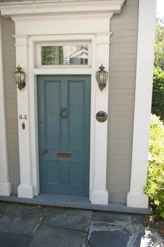 a blue front door on a house with white trim and columns, flanked by two brass knockers