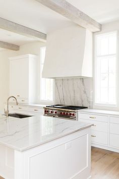 a kitchen with white cabinets and marble counter tops, an oven hood over the stove