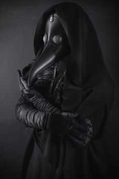 a woman wearing a plague mask and holding a glove in front of her face with both hands