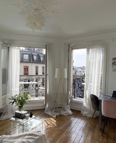 a living room filled with furniture and lots of windows next to a wooden floor covered in white curtains