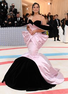 a woman in a pink and black gown standing on a red carpet with people taking pictures behind her