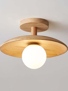 a wooden light fixture with a white ball hanging from it's center point on the ceiling