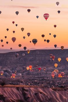 many hot air balloons flying in the sky over a desert landscape at sunset or dawn