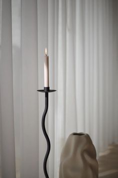 a candle that is on top of a stand in the middle of a room with curtains behind it