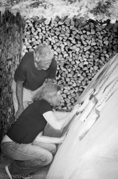 two men are working on a firewood log pile in black and white, while another man is looking at the logs