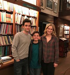 three people standing next to each other in front of a book shelf filled with books