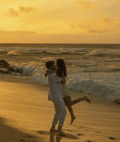 two people are hugging on the beach at sunset