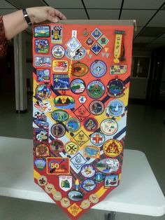 a person holding up an orange banner with many different badges on it, in front of a white table