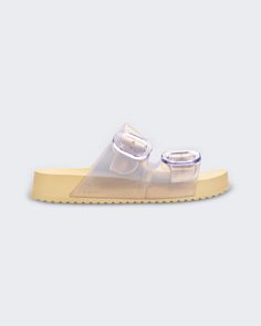 An outer side view of a pearly yellow Melissa Cozy slide on a gray background Trendy Adjustable Sandals For Everyday, Spring Jelly Sandals With Buckle Closure, Summer Style Flat Jelly Sandals With Buckle Closure, Summer Flat Jelly Sandals With Buckle Closure, Summer Jelly Sandals With Buckle Closure, Casual Spring Slides With Tang Buckle, Casual Flat Footbed Sandals With Tang Buckle, Trendy Jelly Slide Sandals With Buckle Closure, Trendy Flat Sandals With Buckle Closure