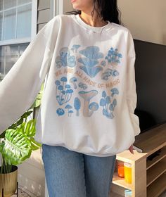 a woman standing in front of a window wearing a white shirt with blue mushrooms on it