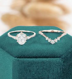 two diamond rings sitting on top of a green velvet box with a ring in the middle