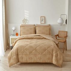 a bed in a room with a beige comforter and pillows on the floor next to a chair