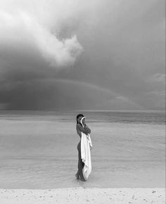 a woman standing on top of a beach next to the ocean under a cloudy sky