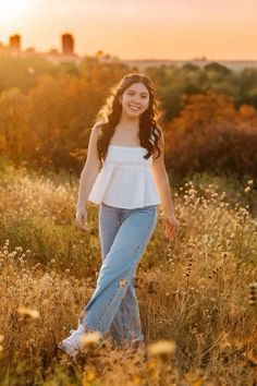 a young woman is walking through the tall grass with her hands in her pockets and smiling at the camera