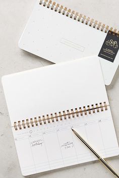 an open spiral bound planner next to a pen and pencil on a white counter top