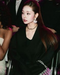 a woman with long hair sitting in a chair at a fashion show, looking off to the side