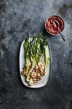 a white plate topped with green vegetables next to a small bowl of ketchup