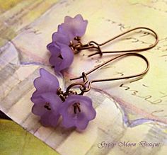 two purple flowers are attached to some metal earwires on a piece of paper