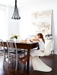 a woman sitting at a table in front of a large piece of art on the wall