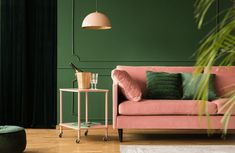 a pink couch sitting next to a green wall and a table with some plants on it