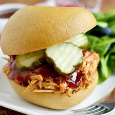 a pulled pork sandwich with cucumbers and ketchup on a plate next to some lettuce