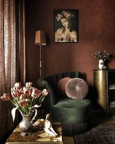 a living room filled with furniture and flowers on top of a coffee table in front of a painting