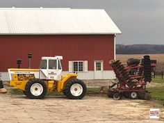 a tractor pulling a trailer full of hay in front of a red barn and silo