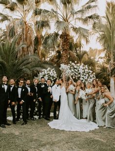 a group of people standing next to each other in front of palm trees and flowers