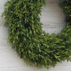 a green wreath hanging on the side of a white wooden wall with no one around it