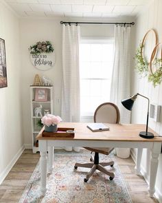 a home office with a desk, chair and rug in front of a window that has white curtains