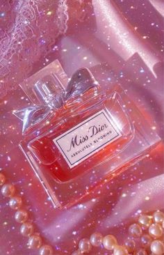 a bottle of miss dior perfume sitting on top of pearls and other items in front of a pink background