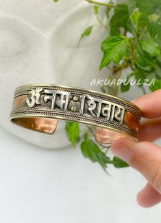 "Introducing our Handmade Mantra Bracelets, lovingly crafted in Nepal by skilled artisans who have brought our vision to life. Elevate your style with these timeless accessories that seamlessly merge the essence of hippie and boho aesthetics, designed for free-spirited souls. 🌿 PRODUCT DETAILS: - Handcrafted in Nepal - Made from Copper, Brass and Pewter (tin, copper, antimony alloy) - Unisex design, perfect for all - Free size and adjustable for a comfortable fit 🌿 UNLOCK THE POWER OF \"OM NAMAH SHIVAYA\" MANTRA: Discover the spiritual significance of the \"Om Namah Shivaya\" mantra, written in Sanskrit, encompassing the essence of unity with its \"Namah\" signifying \"I bow down to\" and \"Shivaya\" representing \"Shiva\" and our inner self.  This mantra's five syllables symbolise the f Round Brass Spiritual Bracelets, Spiritual Round Brass Bracelets, Artisan Handmade Bracelets For Meditation, Adjustable Traditional Bracelets For Rituals, Handmade Symbolic Bangle Bracelets, Handmade Adjustable Spiritual Bangle, Adjustable Round Spiritual Bangle, Handmade Adjustable Bangle For Ceremonial Occasions, Artisan Bangle For Festivals As A Gift