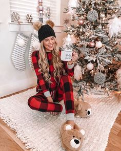 a woman sitting on the floor holding a coffee mug in front of a christmas tree