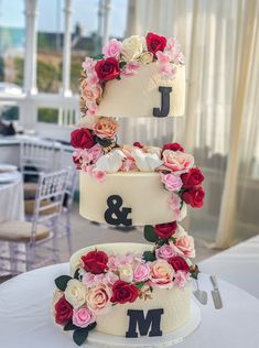 a three tiered cake with flowers on the top and initials on the bottom, sitting on a table