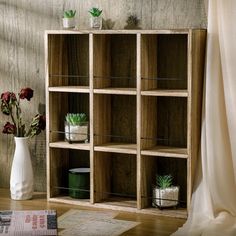 a wooden shelf filled with plants next to a white vase and rug on top of a hard wood floor