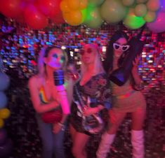 three beautiful women standing next to each other in front of balloons and disco balls at a party