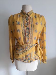 Vintage 80's semi sheer yellow silk shirt, blouse, with a floral print in shades of teal and pink.   A matching silk triangle that can be used as a scarf or a belt makes the set. Ovesized shoulders with small, soft shoulder pads and long sleeves with cuffs. Button up front with small golden lucite buttons. No tags, but it dresses a size M/L, depending on the desired fit. Please check measurements for accuracy: Shoulders: 40cm/15.8" Bust: 102cm/40.1" Length: 58cm/22.8" Sleeve: 59cm/23.2" In very Yellow Floral Print Silk Tops, Yellow Silk Top With Floral Print, Yellow Floral Print Silk Blouse, Yellow Silk Blouse With Floral Print, Vintage Printed Silk Tops, Yellow Bohemian Blouse For Daywear, Vintage Fashion Long Sleeve Summer Blouse, Vintage Fashion Summer Long Sleeve Blouse, Summer Vintage Fashion Long Sleeve Blouse