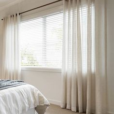 a white bed sitting next to a window in a room with curtains on the windowsill