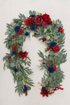 a wreath with red, white and blue flowers on top of green leaves in the shape of an oar