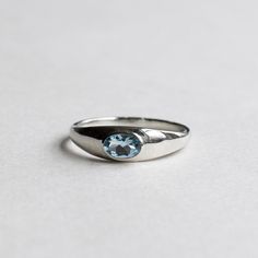 a silver ring with a blue topazte stone in the center on a white surface