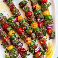 skewers of meat and vegetables on a plate with pesto, lemon wedges