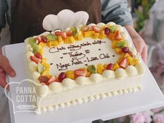 a person holding a cake with fruit on it