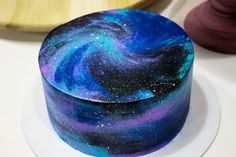 a blue and purple galaxy cake sitting on top of a white plate