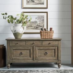 a wooden dresser with two baskets on top of it next to a painting and potted plant