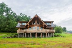 a large wooden house sitting on top of a lush green field next to a forest