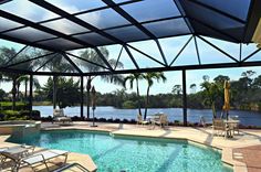 an outdoor swimming pool with chairs and tables next to the water, surrounded by palm trees