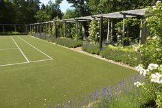 a tennis court surrounded by purple flowers and greenery with trees in the back ground