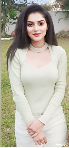 a woman with long black hair wearing a white dress and posing for a photo in the grass