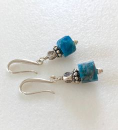 Raw petrol blue apatite earrings with Thai fine silver accents on artisan solid sterling silver ear hooks. Beautiful greenish blue natural apatite faceted gemstone cubes are 9mm and accented with Karen Hill Tribe fine silver triangular beads and sterling silver. Gemstones hang from handmade artisan solid .925 sterling silver ear hooks. Total drop is 1 1/4 inches. Perfect pop of eye catching blue on short artsy ear wires! Turquoise Apatite Gemstone Earrings, Blue Apatite Gemstone Earrings, Blue Apatite Earrings For Gift, Blue Apatite Earrings Gift, Handmade Blue Apatite Earrings, Blue Earrings For Gift, Turquoise Gemstone Earrings, Aquamarine Earrings, Greenish Blue