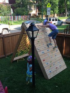 two children playing on a climbing wall made out of wood planks in the backyard